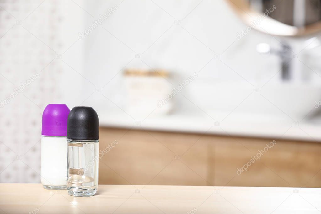Roll-on deodorants on wooden table in bathroom, space for text