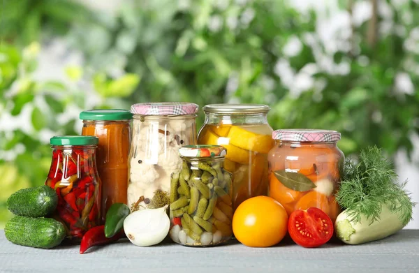 Färska grönsaker och burkar med inlagda produkter på träbord — Stockfoto