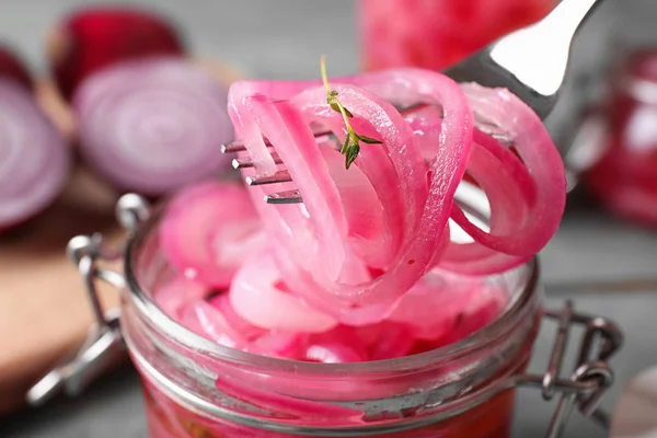 Fork with tasty pickled onion slices over jar on table, closeup