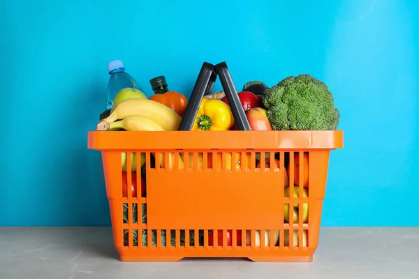 Varukorg med livsmedelsprodukter på grått bord mot ljusblå bakgrund — Stockfoto