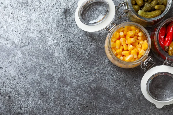 Плоска композиція з баночками з маринованих овочів на сірому столі. Простір для тексту — стокове фото