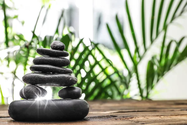 Table with stack of stones and blurred green leaves on background, space for text. Zen concept — Stock Photo, Image