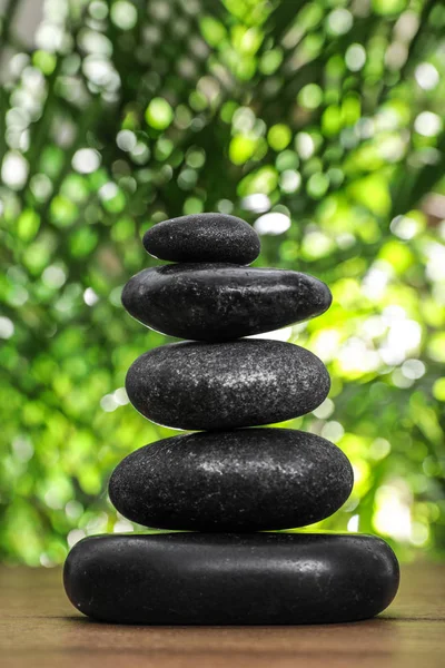Table with stack of stones and blurred green leaves on background. Zen concept — Stock Photo, Image
