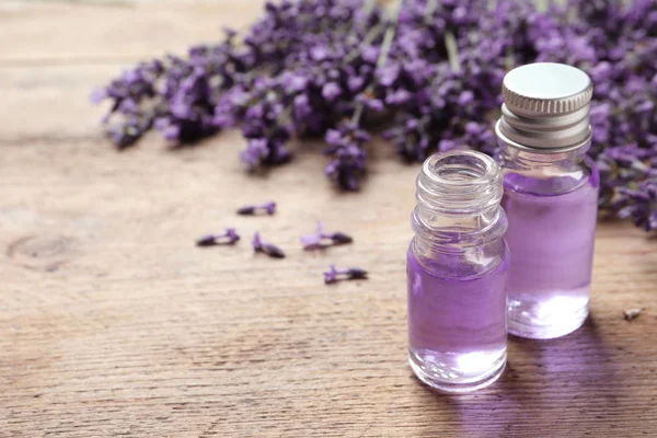 Botellas de vidrio de aceite cosmético natural y flores de lavanda en mesa de madera, espacio para el texto — Foto de Stock