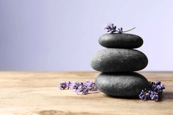 Spa stones and lavender flowers on wooden table against grey background, space for text.