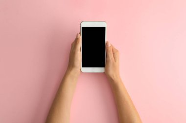 Pembe arka planda modern bir telefon tutan kadın, üst tegörüş. Metin için alan