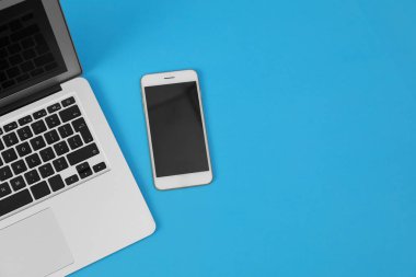 Mavi arka planda modern dizüstü bilgisayar ve akıllı telefon, üst görünüm. Metin için alan