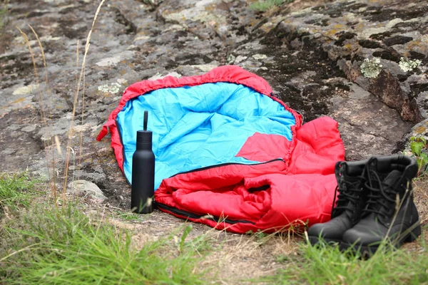 Bolsa de dormir, botas y botella al aire libre. Equipo de camping — Foto de Stock