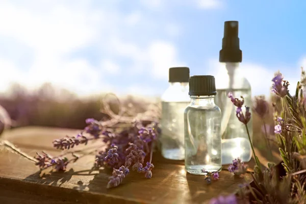 Bottles of lavender essential oil on wooden table in field. Space for text — Stock Photo, Image