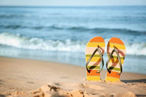 Chanclas con estilo en la arena cerca del mar, espacio para el texto. Accesorios de playa —  Fotos de Stock