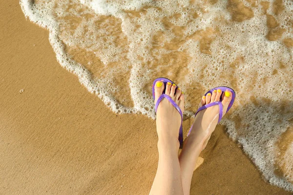 Close-up van de vrouw met flip flops op zand in de buurt van zee, ruimte voor tekst. Strand accessoires — Stockfoto
