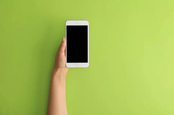 Woman holding modern phone on green background, top view. Space for text