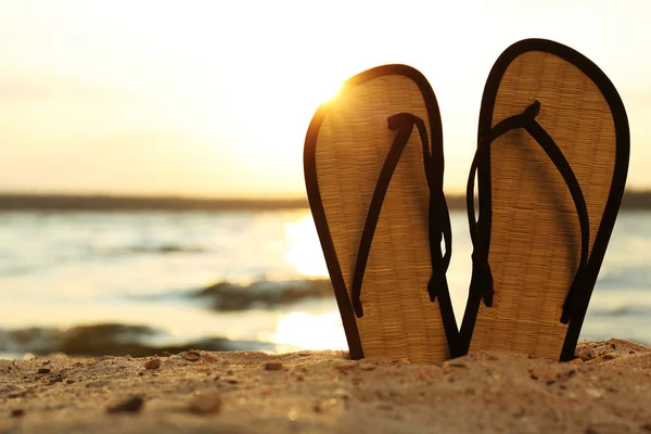 Des tongs élégantes sur le sable près de la mer, espace pour le texte. Accessoires de plage — Photo