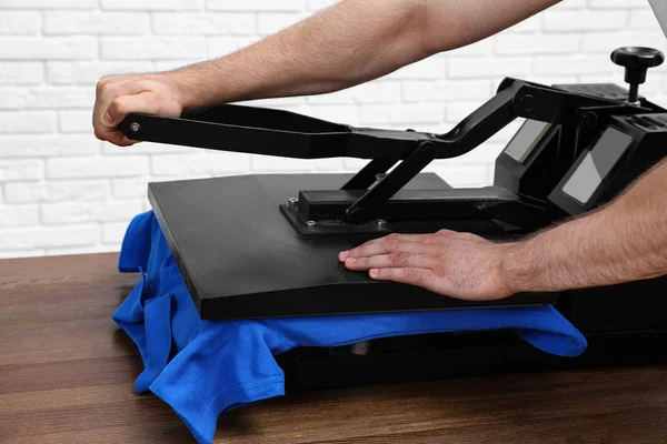 Man using heat press machine at table near white brick wall, closeup