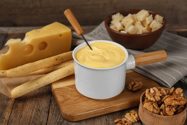 Pot of tasty cheese fondue and products on wooden table