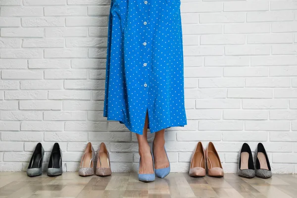 Kvinna som försöker på olika skor nära vit tegelvägg, närbild — Stockfoto