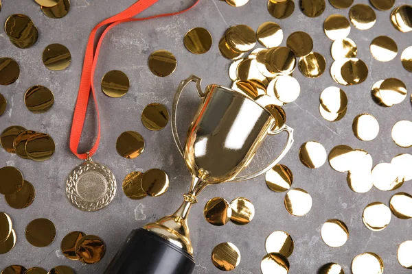 Arany trófea kupa, érem és konfetti a szürke kő háttér, lapos feküdt — Stock Fotó