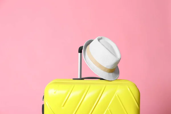 Moderner gelber Koffer und Hut auf hellrosa Hintergrund — Stockfoto