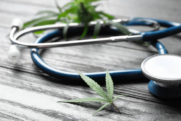 Hemp leaves and stethoscope on grey wooden table, closeup — Stock Photo, Image