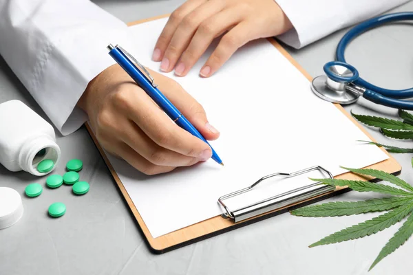 Kvinnlig läkare med Urklipp, piller och hampa blad på grått bord, närbild — Stockfoto