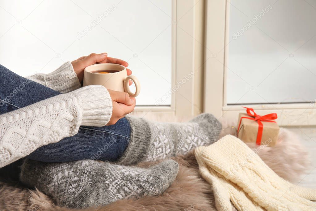 Woman with cup of hot mulled wine sitting on window sill, closeup. Winter drink