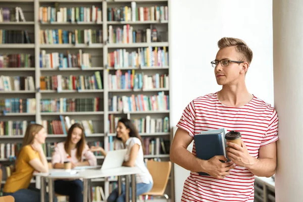 Jovem com livros e bebida na biblioteca. Espaço para texto — Fotografia de Stock