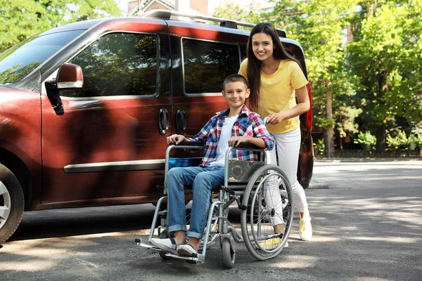 Young woman with boy in wheelchair near van outdoors — Stock Photo, Image