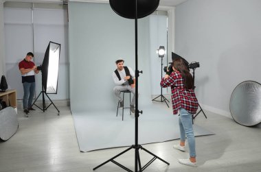 Asistan modern stüdyoda genç adamın fotoğrafını çeken profesyonel fotoğrafçı