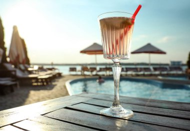 Glass of fresh summer cocktail on wooden table near swimming pool outdoors, low angle view clipart