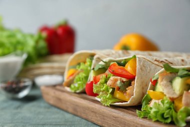 Gri arka plan karşı mavi ahşap masa üzerinde lezzetli et tortilla sarar ile Kurulu, closeup