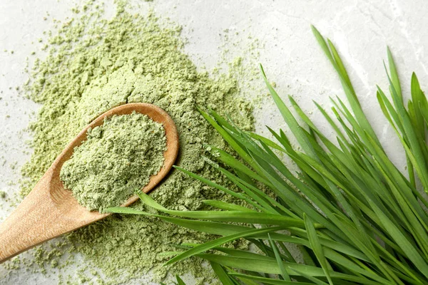 Spoon with wheat grass powder and sprouts on grey table, flat lay