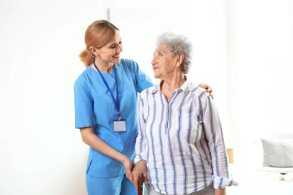 Enfermeira em uniforme assistindo mulher idosa dentro de casa — Fotografia de Stock