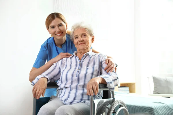 Infirmière aidant femme âgée en fauteuil roulant à l'intérieur — Photo