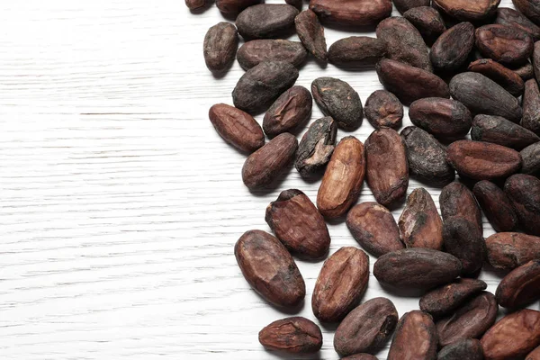 Sabrosos granos de cacao en la mesa de madera blanca, por encima de la vista. Espacio para texto —  Fotos de Stock