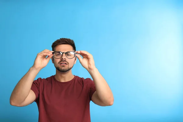 Mladý muž s potížemi se zrakovými brýlemi na modrém pozadí, prostor pro text — Stock fotografie