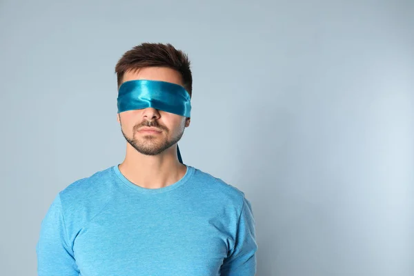 Young man with light blue blindfold on grey background, space for text — Stock Photo, Image