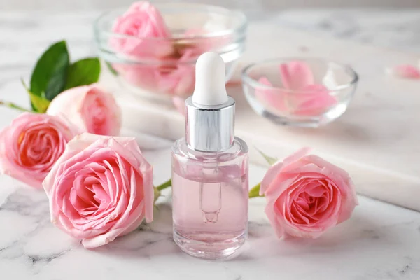 Botella con aceite esencial de rosa y flores sobre mesa de mármol —  Fotos de Stock