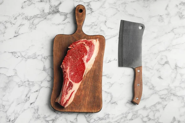 Board with fresh raw beef meat and butcher knife on white marble table, flat lay — Stock Photo, Image