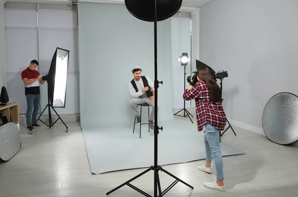Professional photographer with assistant taking picture of young man in modern studio — Stock Photo, Image