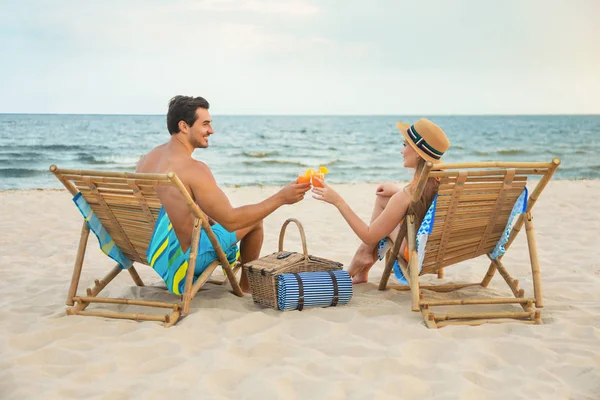 愉快的年轻夫妇与鸡尾酒坐在甲板椅在海滩 — 图库照片