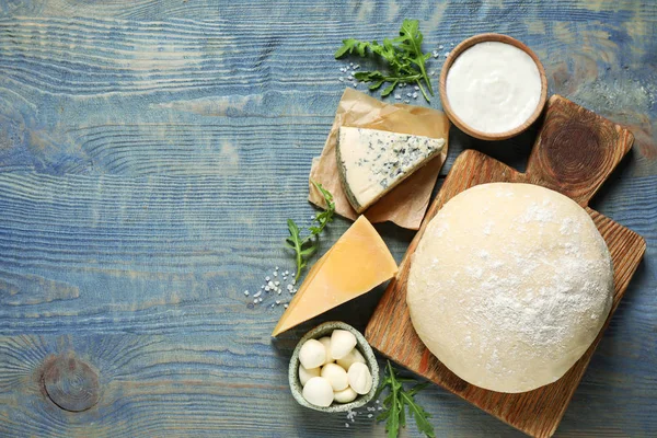 Composição de leigos planos com massa e ingredientes de pizza fresca na mesa de madeira azul. Espaço para texto — Fotografia de Stock