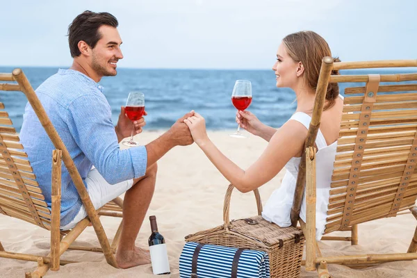Jovem casal feliz com copos de vinho sentado em cadeiras na praia do mar — Fotografia de Stock