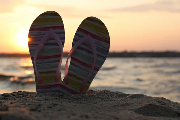 Des tongs élégantes sur le sable près de la mer, espace pour le texte. Accessoires de plage — Photo