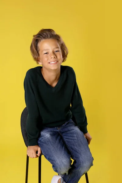 노란색 배경에 의자에 앉아 귀여운 소년 — 스톡 사진