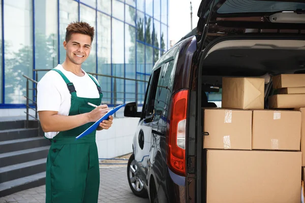 Jovem mensageiro segurando prancheta perto da van de entrega com parcelas ao ar livre — Fotografia de Stock