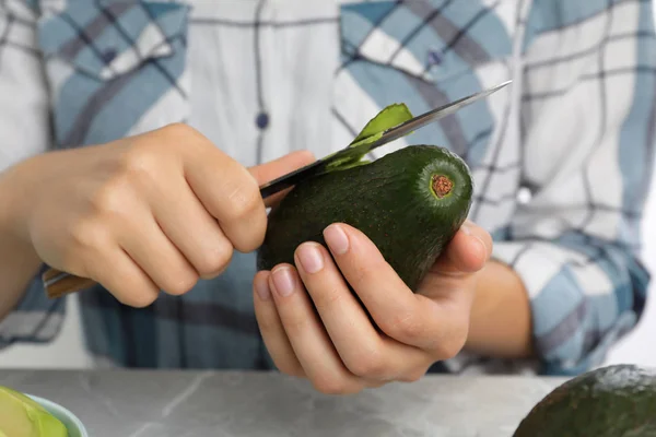 Mujer pelando aguacate maduro en la mesa, primer plano — Foto de Stock