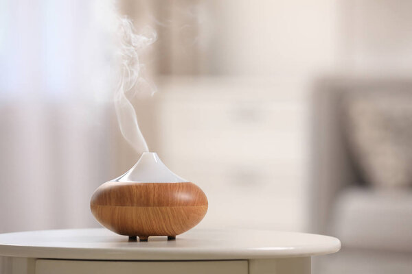 Modern essential oil diffuser on table indoors. Space for text