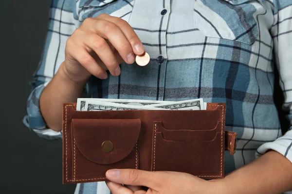 Νεαρή γυναίκα βάζοντας κέρμα σε πορτοφόλι σε γκρι φόντο, κοντινό πλάνο — Φωτογραφία Αρχείου