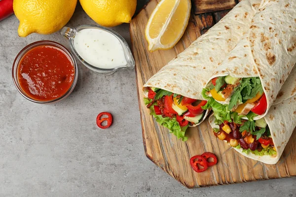 Board with delicious meat tortilla wraps on grey table, flat lay — Stock Photo, Image