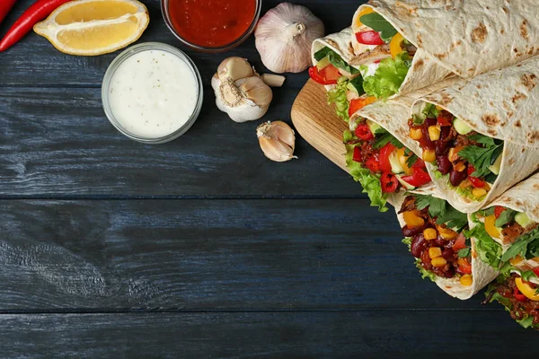 Bord met heerlijke vlees tortilla wraps op blauwe houten tafel, platte lag. Ruimte voor tekst — Stockfoto